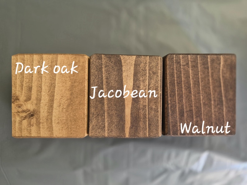 May include: Three wooden blocks with different stain colors: Dark Oak, Jacobean, and Walnut. Each block has the stain name in white text. The wood grain is visible, showcasing the natural texture and color variations of the wood.