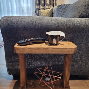 May include: A wooden side table with a shelf, featuring a black and white coffee mug, a remote control, and a copper star-shaped candle holder.