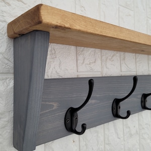 May include: A grey wooden wall-mounted shelf with five black metal hooks. The shelf has a natural wood top and is painted grey.