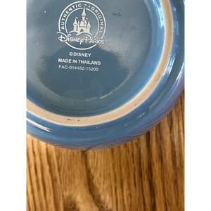 Puede incluir: Taza de cer&aacute;mica azul con un logotipo blanco de Disney Parks y el texto "Authentic Original" alrededor del logotipo. La taza tambi&eacute;n tiene el texto "&copy;Disney Hecho en Tailandia FAC-014182-15200".