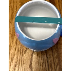 Puede incluir: Una taza de cer&aacute;mica azul con corazones rosas y un interior blanco. La taza tiene un asa en el lado derecho.