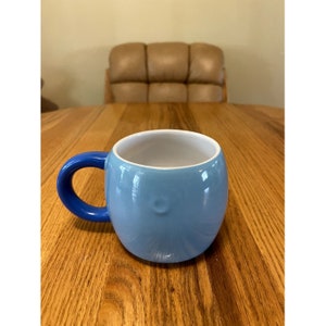 Puede incluir: Una taza de cer&aacute;mica azul claro con un asa azul. La taza tiene una forma redondeada y un interior blanco.