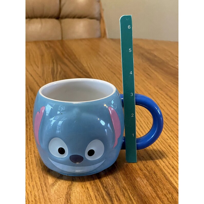 Puede incluir: Una taza de cer&aacute;mica azul con un dise&ntilde;o de personaje de Stitch. La taza tiene un asa azul y orejas rosas. La taza mide 10 cm de alto.