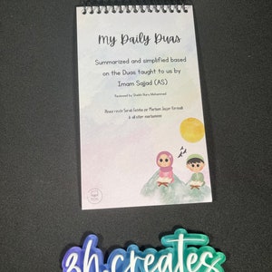 Puede incluir: Un pequeño libro en espiral con una portada colorida que presenta una ilustración de dibujos animados de dos niños leyendo. El título del libro es "My Daily Duas" y el texto de la portada explica que el libro contiene duas resumidos y simplificados enseñados por Imam Sajjad (AS).