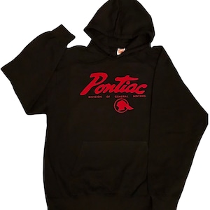 Op de afbeelding: Zwart hoodie met een rood "Pontiac" logo en de tekst "Division of General Motors" eronder. Het logo heeft een rood silhouet van een Indiaans hoofd.