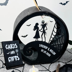 May include: A black and white wedding card box with a silhouette of a couple holding hands, bats, and a spiderweb design. The box has a slot for cards and gifts, with the words "CARDS AND GIFTS" on a small sign.
