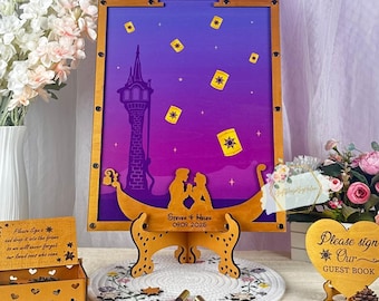 May include: A wooden guest book alternative with a purple and blue background featuring a tower and floating lanterns. The wooden frame has a boat-like design with a stand. Includes a wooden box, pens, and a heart-shaped sign that says "Please sign our guest book".