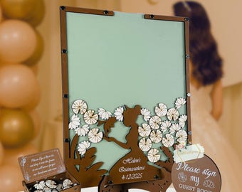 May include: A wooden Quinceañera guest book set. The set includes a large sign with a silhouette of a girl, a box of wooden tokens, and a small sign that says "Please sign my guest book". The large sign has the text "Helen's Quinceañera 4-12-2025".