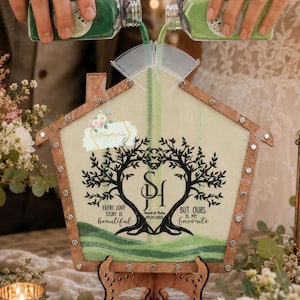 May include: A house-shaped wooden sand ceremony frame with a clear front panel featuring a black tree design, the initials SH, and the text Every love story is beautiful but ours is my favorite, Steven & Helen 09.09.2025, filled with green sand.