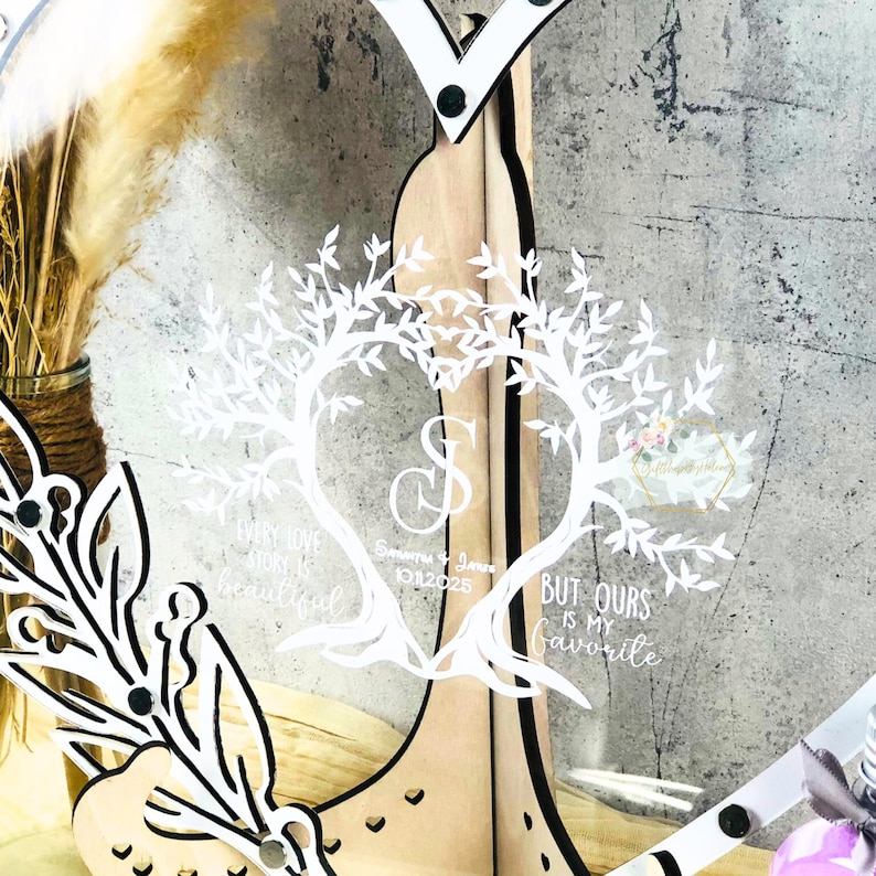 May include: A clear acrylic wedding sign featuring a heart-shaped tree design and the text "Every love story is beautiful, but ours is my favourite." Includes names and a date. The sign is set on a wooden frame.
