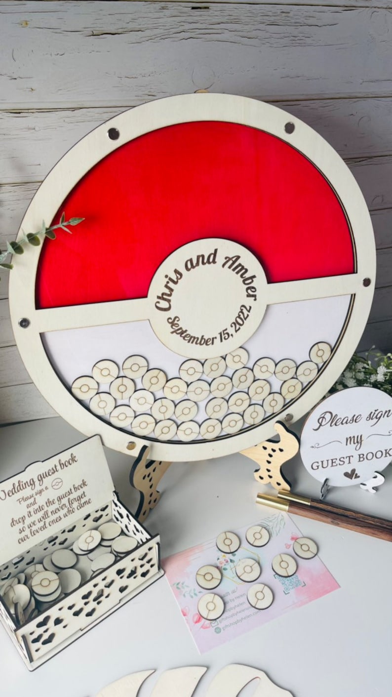 Puede incluir: Un libro de visitas de boda de madera con forma de c&iacute;rculo rojo y blanco con los nombres "Chris and Amber" y la fecha "September 15, 2022". Incluye una caja de fichas de madera para que los invitados firmen y dejen caer en el libro. Un letrero dice "Please sign my GUEST BOOK".