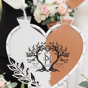 May include: A heart-shaped unity sand ceremony set. One side is filled with white sand, the other with orange sand. The set has a decorative tree design with the text "Every love story is beautiful, but ours is my favourite."