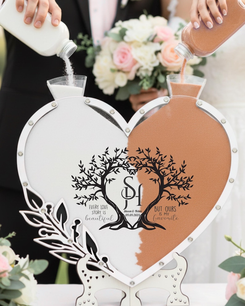 May include: A heart-shaped unity sand ceremony set. One side is filled with white sand, the other with orange sand. The set has a decorative tree design with the text "Every love story is beautiful, but ours is my favourite."