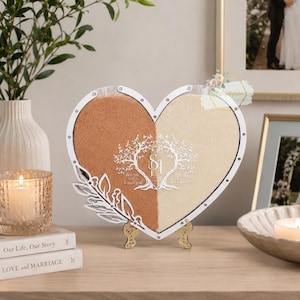 May include: A heart-shaped sand ceremony shadow box with a white frame, divided into two sections filled with tan and cream-coloured sand. The design includes a tree graphic and the text "Best Day Ever, Beautiful". It stands on a gold-coloured stand.