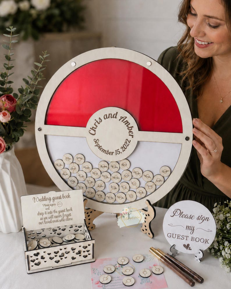 Puede incluir: Un libro de visitas de boda de madera con un dise&ntilde;o rojo y blanco. Los invitados firman peque&ntilde;os discos de madera que se dejan caer en el libro. Los nombres "Chris y Amber" y la fecha "15 de septiembre de 2022" est&aacute;n grabados. Incluye una peque&ntilde;a caja y un letrero de madera.