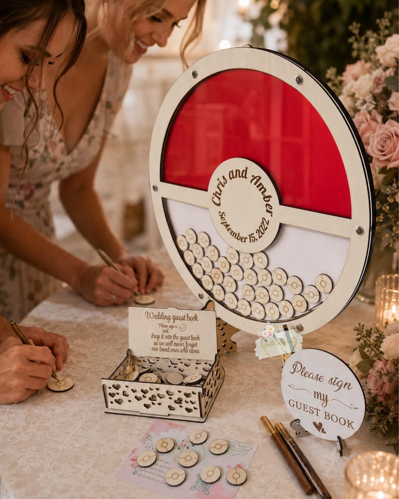 Puede incluir: Libro de visitas de boda de madera con un dise&ntilde;o circular rojo y blanco. Se muestran los nombres "Chris y Amber" y la fecha "15 de septiembre de 2022". Incluye una caja y fichas de madera para firmar.