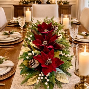 May include: A holiday centerpiece featuring three deep red velvet poinsettia flowers, green pine branches, brown pinecones, and white berry clusters. The arrangement is displayed on a textured table runner with glass candle holders and white candles.