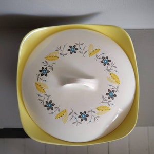 May include: A white ceramic lid with a yellow rim and a floral design. The lid has a handle and is perfect for a vintage casserole dish.