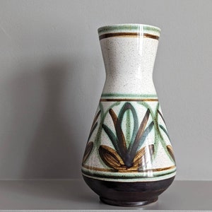 May include: A white ceramic vase with a brown and green floral design. The vase has a wide base and a narrow neck.