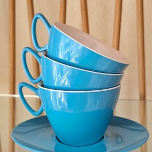 May include: Three blue ceramic teacups stacked on top of each other with a matching blue saucer. The cups have a white rim.