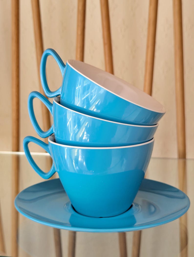 May include: Three blue ceramic teacups stacked on top of each other with a matching blue saucer. The cups have a white rim.