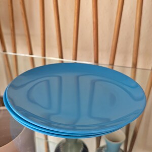 May include: A stack of three blue ceramic plates. The plates are round and have a smooth, glossy finish.