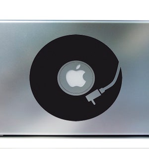 May include: A silver laptop with a black vinyl record design. The record features the Apple logo at its center and a tone arm graphic. The design is a sticker or decal applied to the laptop's surface.
