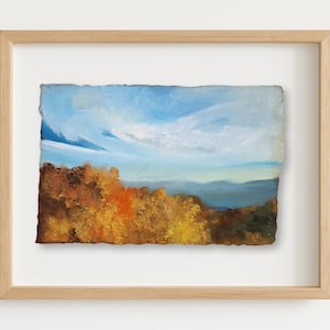 May include: An original landscape painting in a light wood frame. The artwork depicts a vibrant scene of a blue sky with white clouds over a range of mountains and colorful autumn trees. The painting is on textured paper.