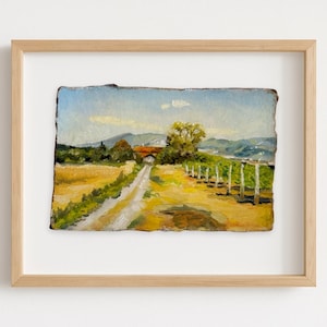 May include: An original landscape painting in a wooden frame. The artwork depicts a rural scene with a dirt road leading to a building with a red roof. The painting features a field of yellow and green, with mountains in the background.