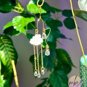May include: Gold earring with a white cloud charm and dangling crystal drops. The earring is hanging from a gold hook.
