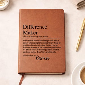 May include: A brown leather journal with the words "Difference Maker" and a definition printed on the cover. The name "Karen" is written below the definition. A gold pen and a cup of coffee are next to the journal.