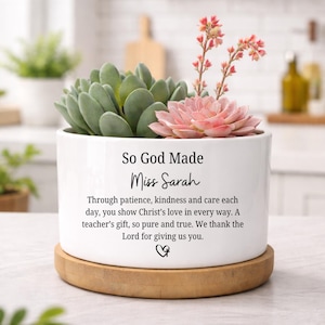 May include: White ceramic planter with a succulent arrangement. The planter has the text "So God Made Miss Sarah" and a message about a teacher. The planter sits on a round wooden base.