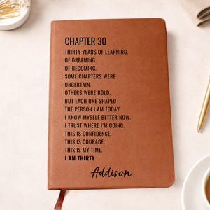 Puede incluir: Un diario de cuero marrón con el texto "CHAPTER 30" y un poema sobre cumplir treinta años. El nombre "Addison" está escrito en la parte inferior. Una cinta roja como marcapáginas es visible.
