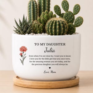 May include: A white ceramic planter with a bamboo saucer containing various green cacti and succulents. The planter features a printed message: TO MY DAUGHTER Julia, followed by a sentimental paragraph, a small heart icon, and the signature Love, Mom.