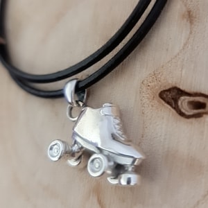 Puede incluir: Un collar con un colgante de patín de ruedas de plata en un cordón de cuero negro.