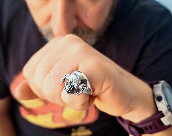 May include: A silver ring featuring a detailed bull design. The ring is worn on a finger, showcasing the intricate craftsmanship of the bull's head and horns. The ring's metallic sheen contrasts with the skin tone, highlighting the jewelry's design.