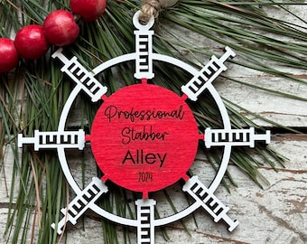 May include: A red and white wooden Christmas ornament shaped like a snowflake with the words "Professional Stabber Alley 2024" in black text.