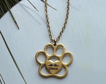 May include: Gold necklace with a paw print pendant featuring a heart with a mustache and the name "Simon" engraved inside.