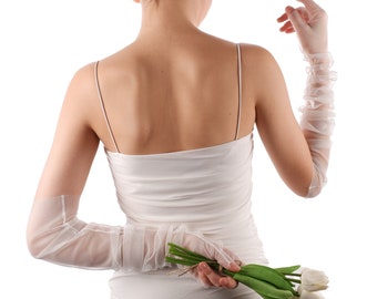 May include: A woman wearing a white dress and long white gloves holds a bouquet of white tulips behind her back.