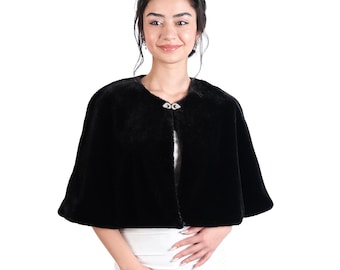May include: A black faux fur shawl with a decorative button closure. The shawl is short and has a rounded neckline.