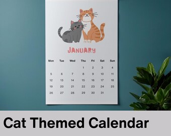 May include: A cat-themed calendar for 2026, featuring illustrations of two cartoon cats. One is gray, and the other is orange with stripes. The month of January is displayed with a weekly calendar grid. The calendar is hanging on a wall.