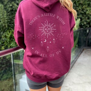 Puede incluir: Sudadera con capucha burdeos con la inscripci&oacute;n blanca "THERE'S A LITTLE WITCH IN ALL OF US". El dise&ntilde;o presenta un sol, estrellas, lunas y cristales. La sudadera es de color liso y tiene un corte holgado.
