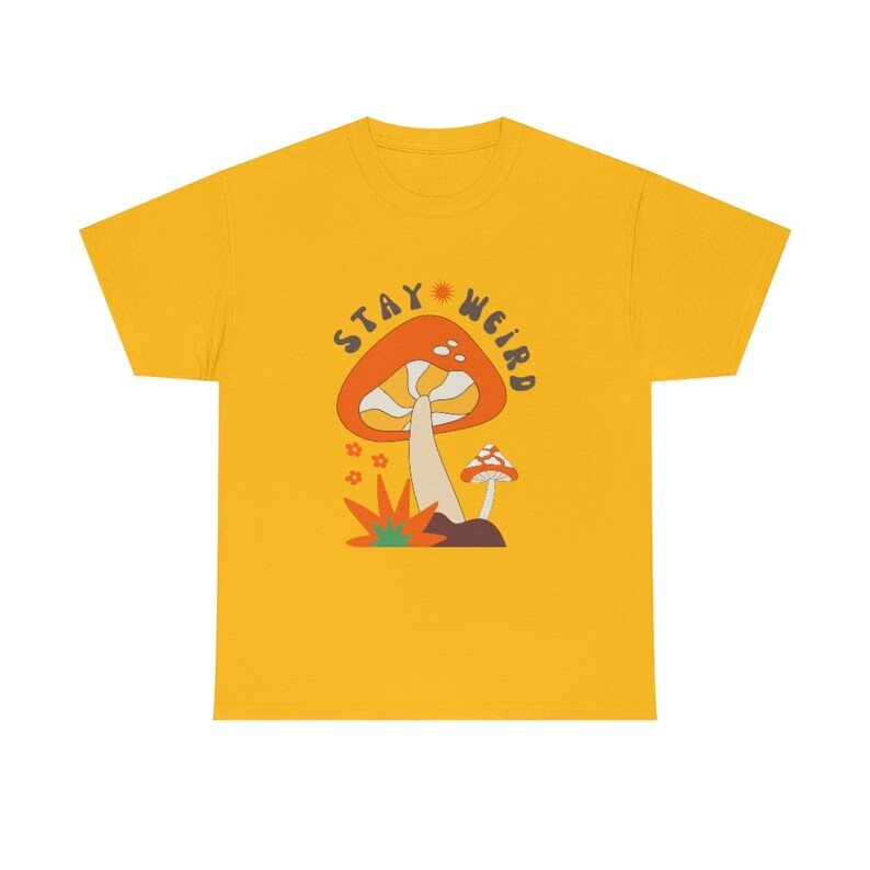 May include: Mustard yellow t-shirt with a retro-style mushroom graphic. The design features a large orange mushroom with white spots, a smaller mushroom, and the text "STAY WEIRD" in a circular arrangement.
