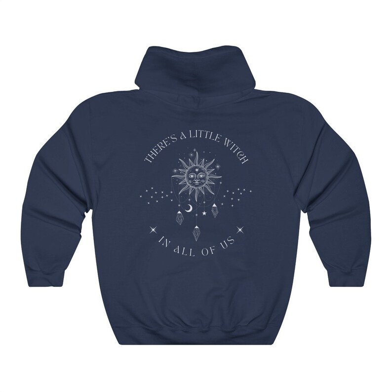 Puede incluir: Sudadera con capucha azul marino con un gr&aacute;fico blanco en la espalda. El gr&aacute;fico presenta un sol, estrellas y el texto "THERE'S A LITTLE WITCH IN ALL OF US."