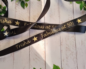 May include: Black satin ribbon with gold stars and the text "Trisha Fabulous at 50!" printed on it.