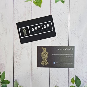 May include: Two business cards with a black background and gold lettering. The top card has the logo "MUNINN PROTECTION SERVICES" with a stylized raven design. The bottom card has the name "Martin Crosfill" and contact information for Muninn Protection Services.