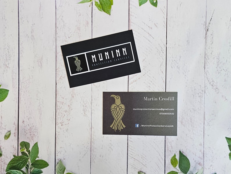 May include: Two business cards with a black background and gold lettering. The top card has the logo "MUNINN PROTECTION SERVICES" with a stylized raven design. The bottom card has the name "Martin Crosfill" and contact information for Muninn Protection Services.