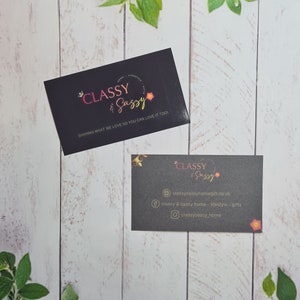 May include: Two black business cards with gold lettering. The top card says "CLASSY & SASSY" and "SHARING WHAT WE LOVE SO YOU CAN LOVE IT TOO". The bottom card says "CLASSY & SASSY" and includes contact information for the business.