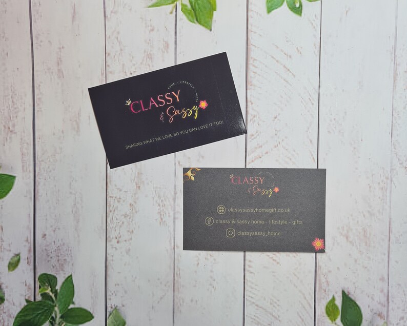 May include: Two black business cards with gold lettering. The top card says "CLASSY & SASSY" and "SHARING WHAT WE LOVE SO YOU CAN LOVE IT TOO". The bottom card says "CLASSY & SASSY" and includes contact information for the business.
