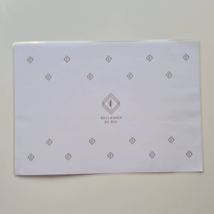Peut inclure: Papier blanc avec un motif répétitif de petits diamants. Au centre du papier se trouve un logo avec une plante stylisée et le texte "RECLAIMED BY RIO".